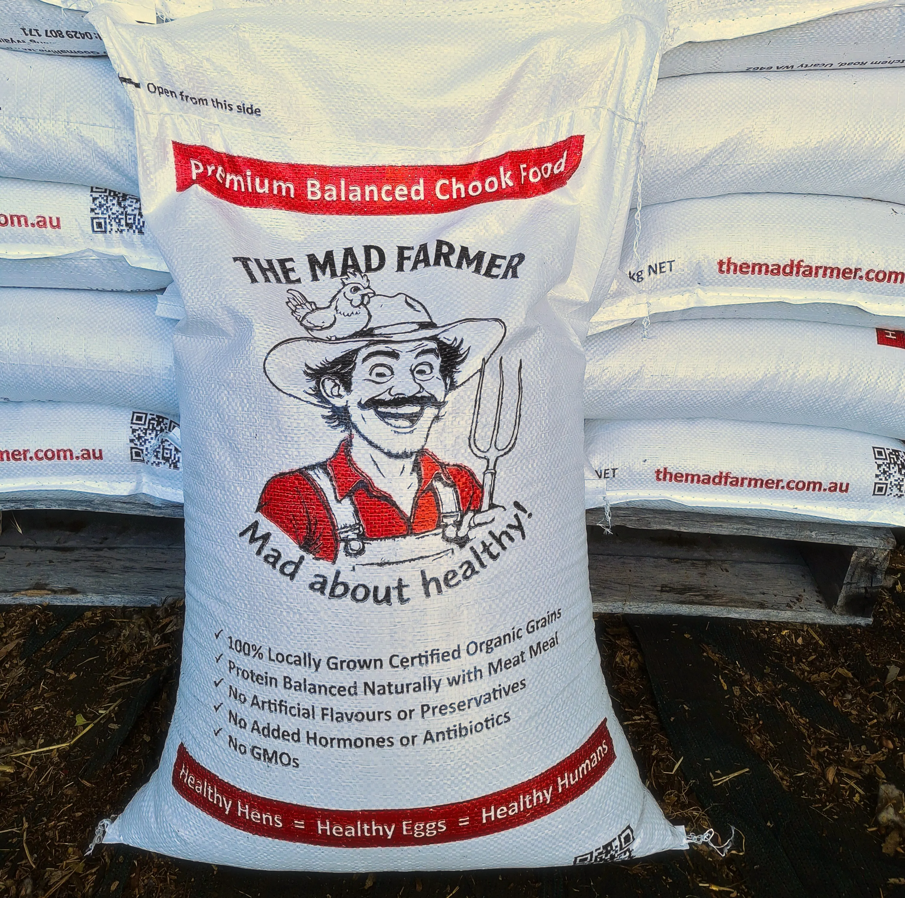 the mad farmer chook food bag resting against a stack of bags behind it.